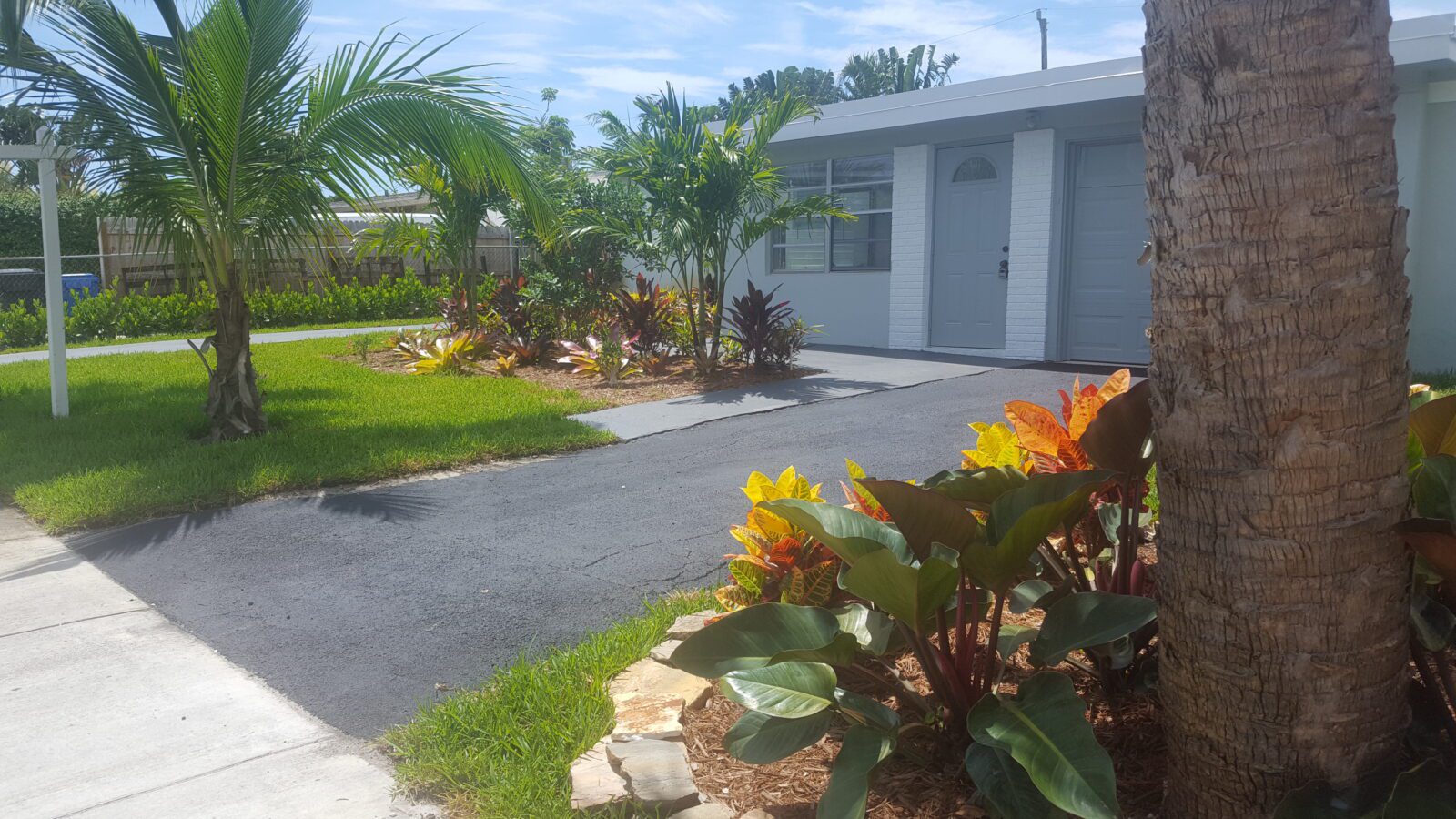 Cozy house entrance with tropical plants and a stone-bordered garden.
