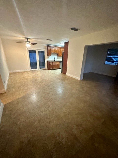 Empty living room with brown flooring and built-in kitchen.