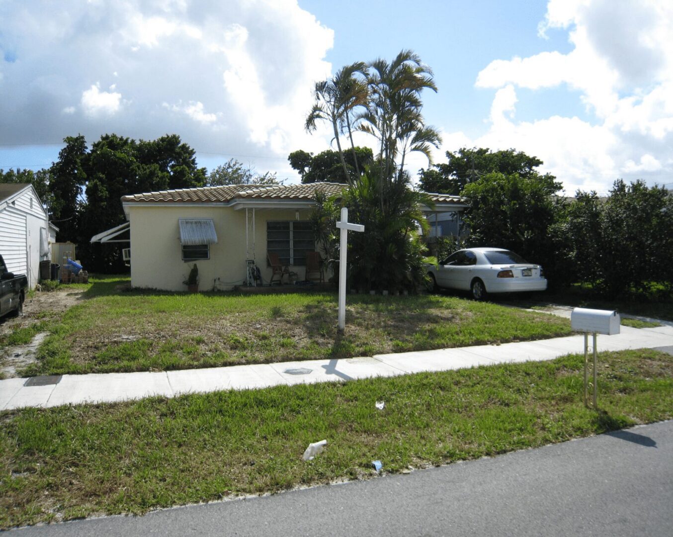 Small house with a front yard and palm trees under a partly cloudy sky.