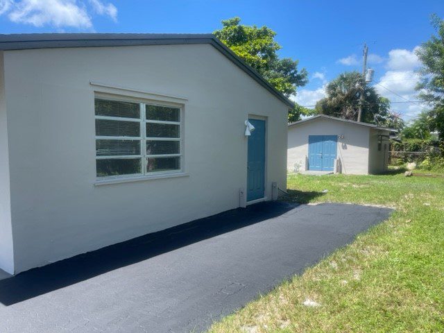 Freshly paved driveway beside two white buildings under a blue sky.