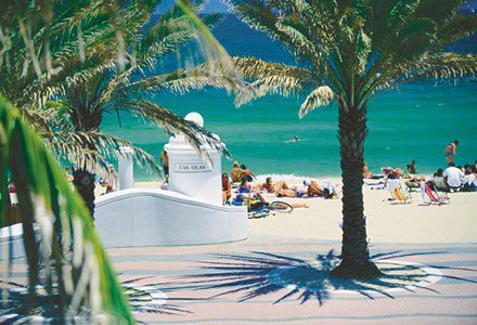 Beach scene with a lifeguard stand, palm trees, and people enjoying the sun and ocean.