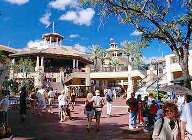 Busy amusement park entrance with visitors under a bright blue sky.